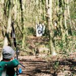 Bogenschütze mit Recurvebogen zielt im Wald auf eine Scheibe