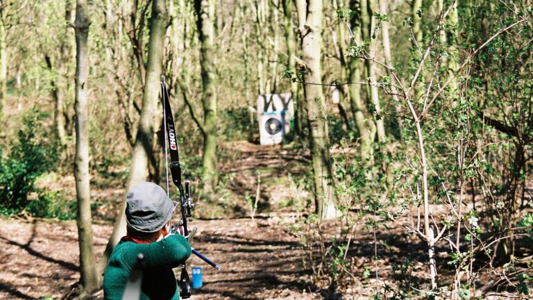 Bogenschütze mit Recurvebogen zielt im Wald auf eine Scheibe